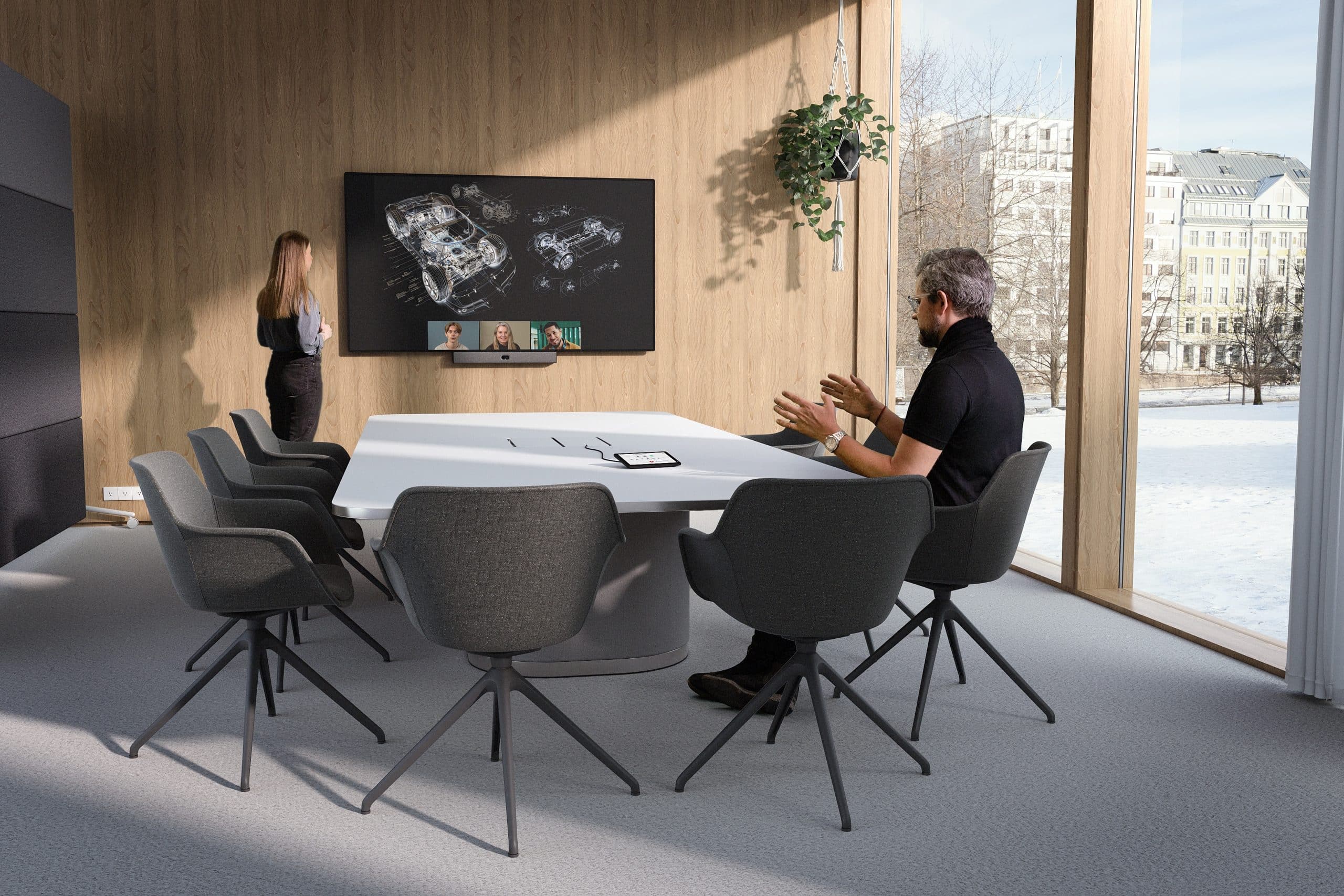 Modern conference room with snowy view—one on video call, another at table with tablet. Stylish gray chairs, wooden accent wall.
